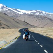 Mountain road in Ladakh with a motorcycle and snow-covered peaks in the distance