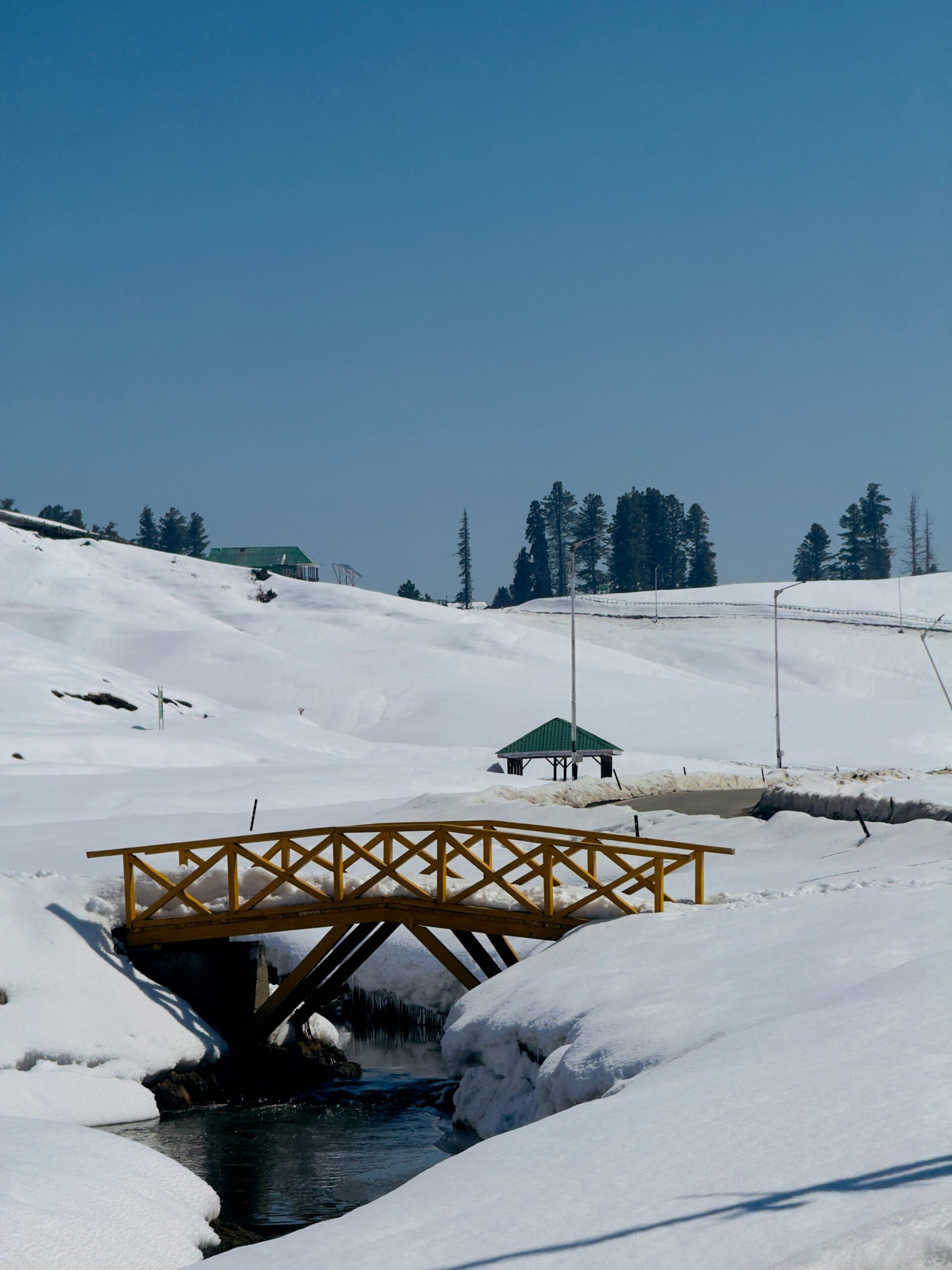 Snow-covered wooden bridge and stream in Gulmarg, Kashmir winter wonderland